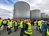 Gæster iført gule refleksveste og røde hjelme foran store reaktortanke på biogasanlæg.
