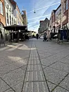 Billedet viser Østre Gågade i retning mod Jernbanepunktet. Det er taget i frøperspektiv, og foran ses flere personer, der kigger på butikker.