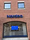 Billedet viser Nordeas filial med en rød murstensbygning, et stort vindue og bankens logo henover med Nordea skrevet i blå bogstaver.