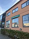 Billedet viser en stor bygning i røde mursten med store vinduespartier. Over det ene vindue er et grønt Jyske Bank-skilt.